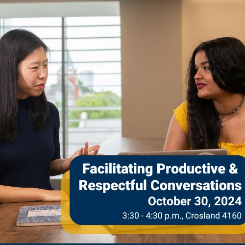 Two students have a conversation while seated at a table.