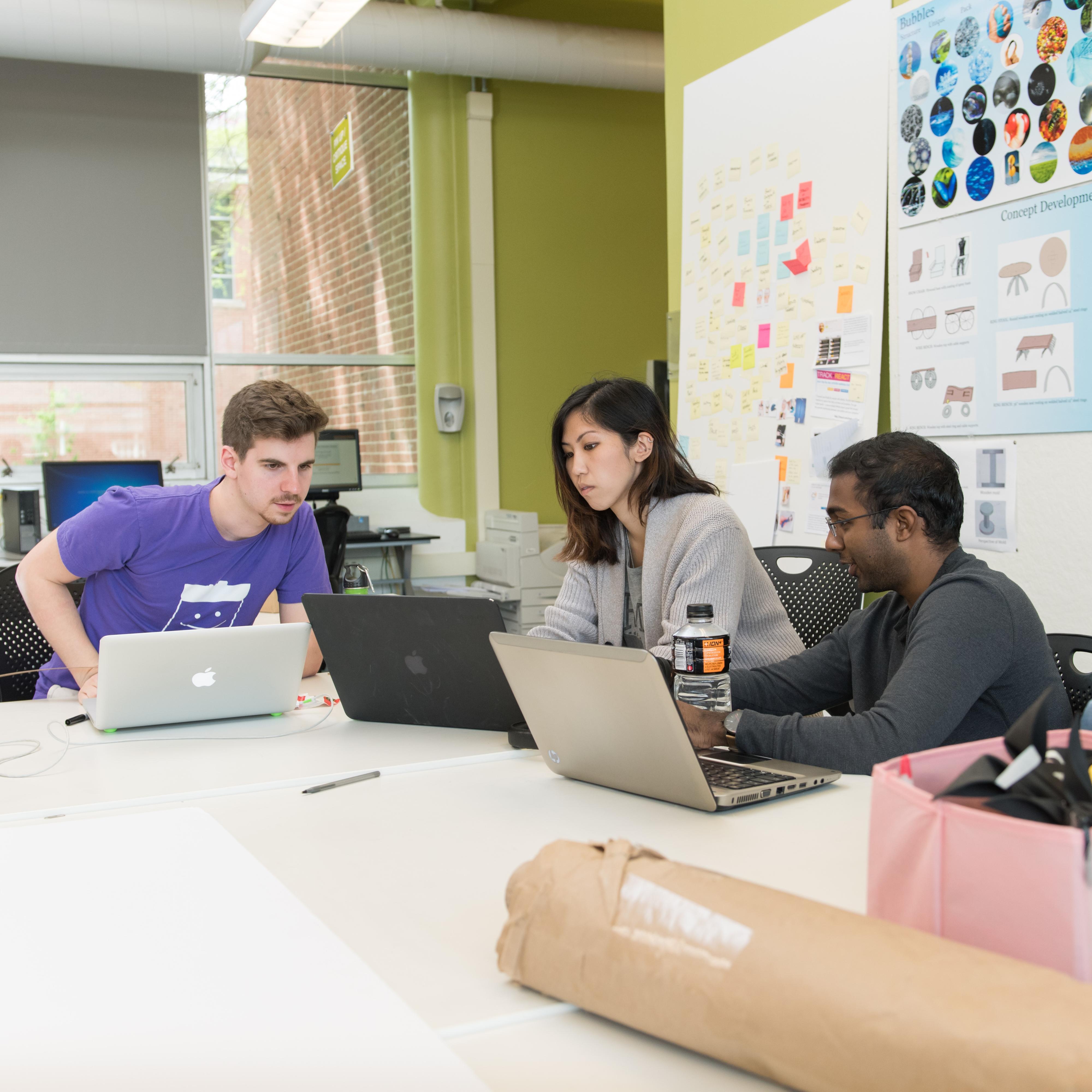 Three people gather around laptops.