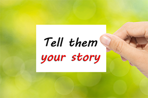 "White paper in front of a blurred green background. Paper reads: Tell them your story."