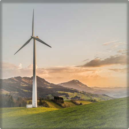 A photo of a windmill (on the left) on a grassy plain with mountains behind it and a sunset.