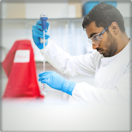 Researcher in a lab using a dropper to put a chemical into a beaker.